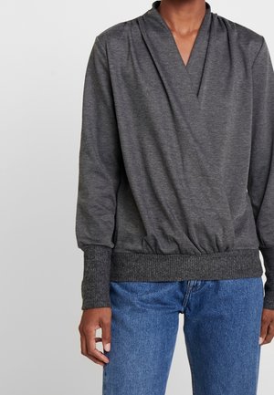 Haut gris à manches longues avec un décolleté en V, texture froncée à la taille et manches ajustées avec poignets, associé à un jean en denim bleu.