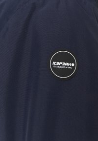 Tecido azul marinho com um retângulo preto circular com o texto branco "ICEPEAK ESTABELECIDO EM 1996." Textura suave, design de vestuário padrão.