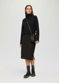 Schwarzer Rollkragenpullover, strukturierter dunkelgrüner Rock mit seitlichem Schlitz, kombiniert mit schwarzen Ankle Boots und einer kleinen schwarzen Umhängetasche.