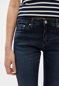 Tmavomodré džínsové nohavice s priliehavým strihom, dizajnom s piatimi vreckami, zlatým kovovým príslušenstvom a malým logom na prednom vrecku.