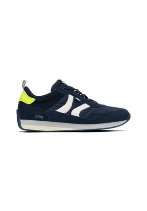 Zapatilla deportiva azul marino con rayas blancas laterales, lengüeta en el talón de color amarillo neón, lazo de sujeción gris, y suela gris y beige, marcada con el número 2003 en el lateral.