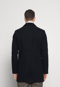 Marineblauer Wollmantel mit tailliertem Schnitt, einreihigem Design, Reverskragen und langen Ärmeln, mit einem sauberen Rücken ohne Verzierungen.