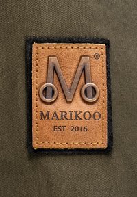 Leather patch with embossed logo and text "MARIKOO EST 2016," bordered by black fabric. Background is dark olive green canvas.