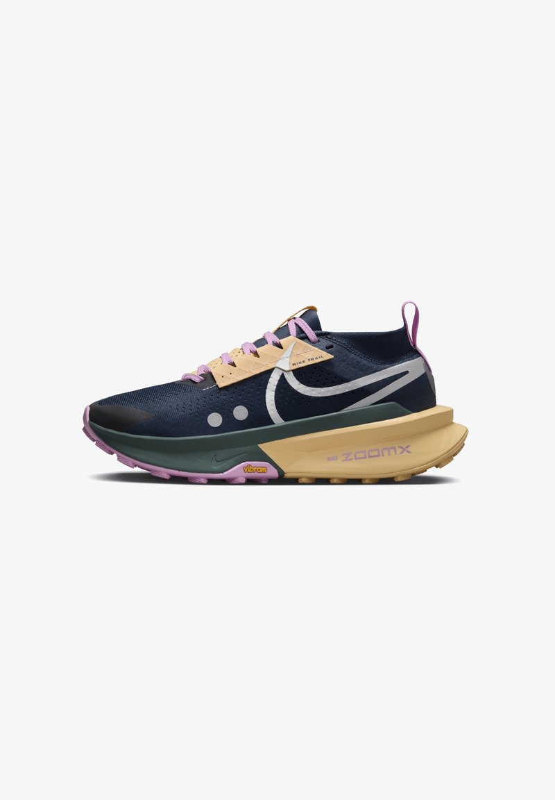 Chaussure de trail Nike bleu marine et beige avec lacets violets, semelle épaisse et logo Swoosh blanc sur le côté, inclinée vers la gauche.