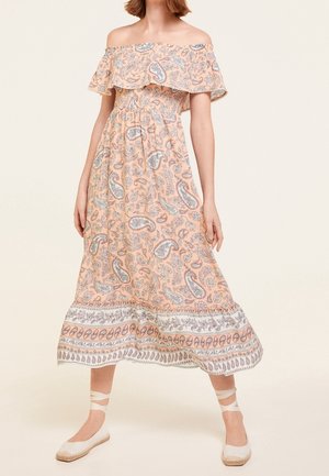 Robe pêche femme épaules dénudées avec motif paisley et détail volanté, associée à des espadrilles blanches avec liens à la cheville.