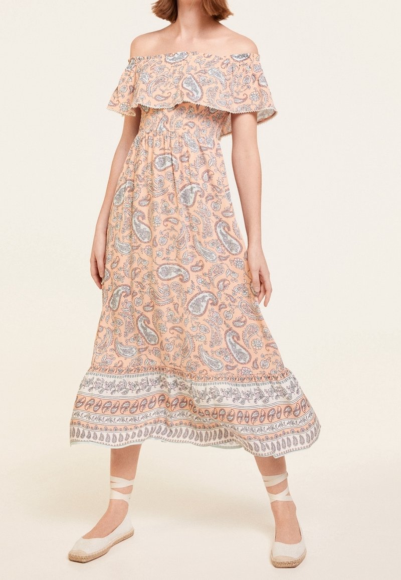 Robe pêche femme épaules dénudées avec motif paisley et détail volanté, associée à des espadrilles blanches avec liens à la cheville.