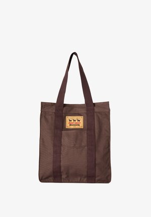Bolsa tote de lona marrón con asas largas de color marrón oscuro y un parche rectangular amarillo con el texto "Jean's West" en el frente.