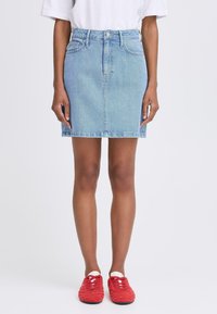 Light blue denim mini skirt with a high waist, front button closure, and seams. Paired with red sneakers featuring textured fabric.