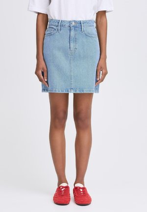 Light blue denim mini skirt with a high waist, front button closure, and seams. Paired with red sneakers featuring textured fabric.