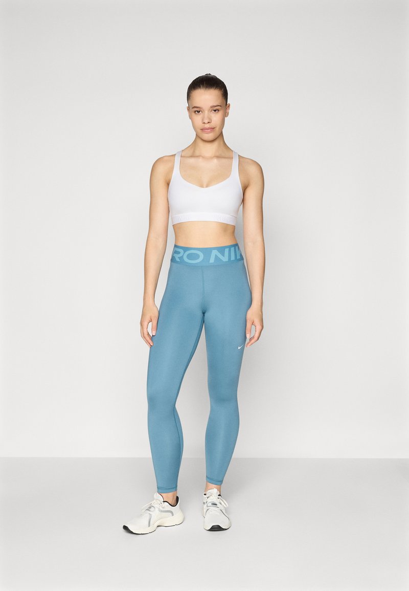 Sujetador deportivo blanco con tirantes ajustables, combinado con leggins de tiro alto en azul claro que presentan el logo "PRO" y una pequeña marca de verificación blanca de Nike.