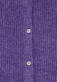 Violets adīts džemperis ar teksturētu rakstu, kurā ir rinda ar baltām pogām priekšpusē un maiga, ērta auduma sajūta.
