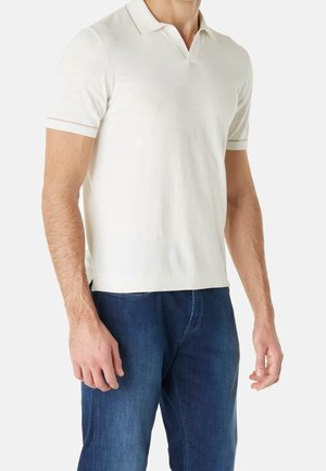 Polo bianca a maniche corte con una texture morbida, dotata di colletto a maglia piatta e bordatura a contrasto sulle maniche. Abbinata a jeans blu scuro.