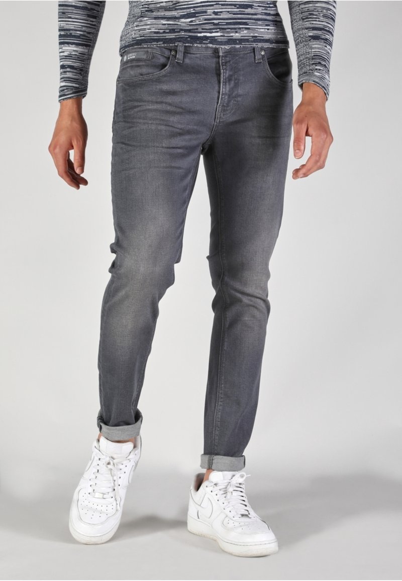 Jeans de mezclilla gris de corte ajustado, con una ligera textura desgastada y puños enrollados, combinados con zapatillas blancas.