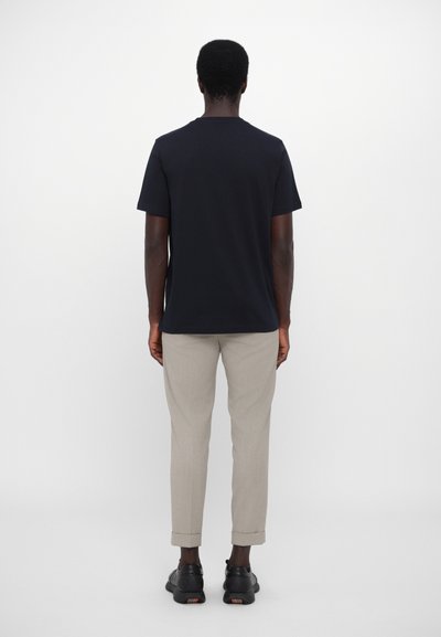T-shirt noire à manches courtes, en tissu de coton, coupe standard, associée à un pantalon gris clair, avec des poignets roulés, et des chaussures noires avec une subtile accent.