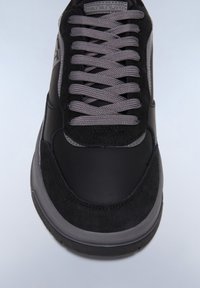 Sneaker nera con materiali in suede e pelle, dotata di lacci e dettagli grigi, punta rotonda e suola ammortizzata.
