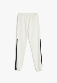 Pantalones de chándal blancos con cinturilla elástica y rayas laterales negras, elaborados en tela suave, con un diseño de pierna ajustada.