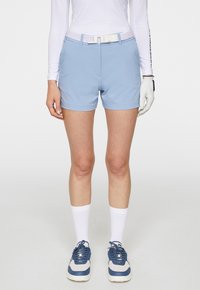 Ljust blå golfshorts med en slät yta, kombinerat med ett vitt bälte med en strukturerad design, och matchat med grå och blå sportskor.
