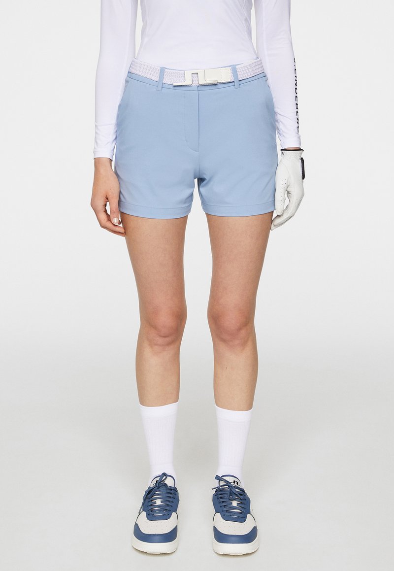 Ljust blå golfshorts med en slät yta, kombinerat med ett vitt bälte med en strukturerad design, och matchat med grå och blå sportskor.