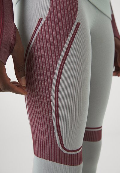 Közelkép sportos leggingsről világoskék színben, bordó csíkos díszítéssel. Az anyag sima textúrájú, a fazonja kontúrozott, és varrásokkal rendelkezik.