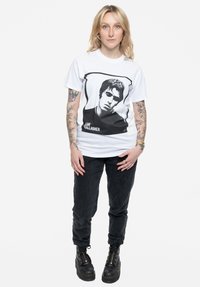 White cotton T-shirt featuring a black graphic of a man’s face, paired with black corduroy pants and black lace-up boots.