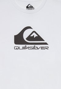 Bijela pamučna majica s velikim crnim Quiksilver logotipom, uz stilizirane dizajne planine i valova. Glatka tekstura, standardni okrugli izrez.