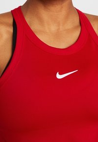 Débardeur de sport rouge en tissu lisse, avec un col côtelé et un logo Nike blanc au centre.