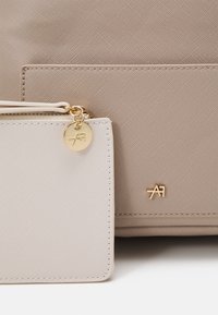 Bolsa texturizada color tabaco con una pequeña billetera a juego. Ambas cuentan con detalles en dorado y un logo, mostrando un acabado liso y líneas limpias.