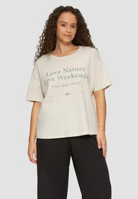 Kurze Ärmel, hellbeige T-Shirt mit grünem Text, der "Liebe die Natur, lebe Wochenenden" und "Besitze deinen Wert" lautet. Boxy-Schnitt und weicher Stoff.
