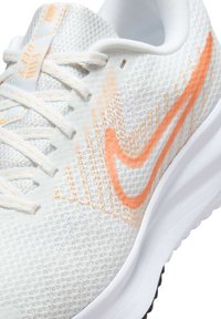 Hvid atletisk sko med orange Nike swoosh, mesh-stof og hvide snørebånd med orange syninger.