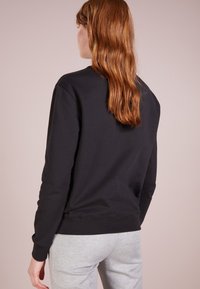 Svart sweatshirt med rund halsringning och långa ärmar, tillverkad av en bomullsblandning, kombinerad med ljusgrå sweatpants.