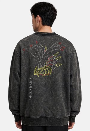 Man draagt een zwarte gewassen trui met een meerkleurig gestileerd drakenmotief en verticale Japanse tekst op de rug.