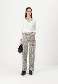 Top blanco de manga larga con textura acanalada y escote en V, combinado con pantalones beige de tiro alto que presentan rayas negras de tigre. Bolso negro y zapatos gruesos.