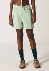 Pantaloni corti verde menta con tasche laterali, vita elastica e vestibilità comoda. Abbinati a calze a coste verde scuro e sneaker color sabbia.
