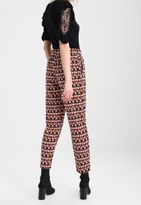 Haut noir avec détails en dentelle sur les manches, associé à un pantalon ajusté à motifs dans des tons terreux, présentant un design géométrique et une longueur jusqu'à la cheville.