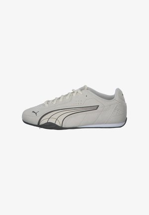 Zapatillas de ante gris claro con acentos negros, con un perfil bajo, punta redondeada y cierre de cordones. Paneles laterales texturizados y detalle del logo.