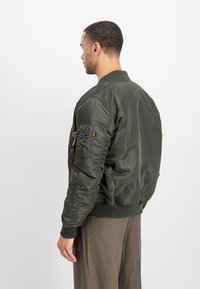 Olive green bomber jacket with ribbed collar and cuffs, shiny fabric, side pocket with zipper, and gathered detailing on sleeves.