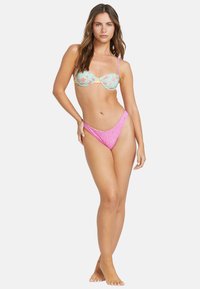 Bikini set s květinovým vzorem, mátově zeleným topem s kosticemi a nastavitelnými ramínky, doplněný o vykrojené plavky s růžovými detaily.