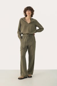 Olijfgroene linnen blouse met een kraag en V-hals, gecombineerd met bijpassende elastische broek met tailleband en donkere sandalen, gepresenteerd op een model.