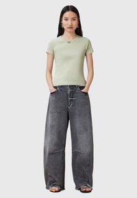 Maglietta aderente verde chiaro abbinata a jeans in denim nero sbiadito, larghi. Caratteristiche notevoli includono un colletto rotondo e un design a gamba larga.