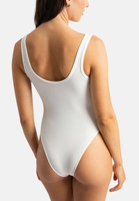 Maillot de bain une pièce blanc côtelé avec des bretelles larges et un design à dos bas, présentant une coupe haute sur les jambes et une couverture minimale à l'arrière.