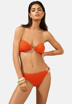 Bikini set in ribbeloranje materiaal; bandeau-top met gouden cirkelhardware in het midden, bijpassende high-waisted onderkant met zijaccenten.