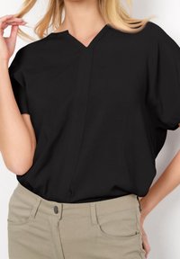Blusa nera a maniche corte con colletto a V e dettagli di cucitura minimal, abbinata a pantaloni di colore chiaro con tasche.