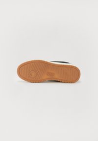 Svart og hvit sneakers med en teksturert gummisåle i brunt. Har et logo og geometrisk mønster på bunnen. Stilig, lavprofilert design.
