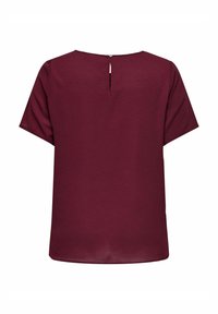 Bordeaux kortärmad topp med rund halsringning och ett nyckelhål i ryggen som stängs med en knapp. Slät textur och avslappnad passform.
