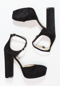 Černé semišové boty na vysokém podpatku s platformovou špičkou, nártní páskem se sponou a masivním blokovým podpatkem s metalickým akcentem.