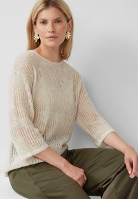 Maglione lavorato a maglia in crema chiaro, con motivo a punto aperto, scollatura tonda e maniche a tre quarti, abbinato a pantaloni verde oliva.
