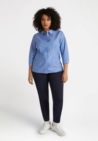Camisa de botones a rayas azul y blanca con cuello y mangas de tres cuartos, combinada con pantalones marino y zapatillas blancas.