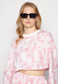Sweatshirt cropped em tie-dye rosa e branco, com mangas longas e um colarinho branco. Combinado com óculos de sol quadrados pretos.
