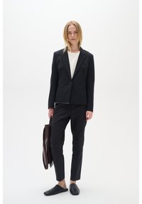 Černý zašitý blazer a odpovídající kalhoty s bílým topem, doplněné černými nazouvacími botami a hnědou koženou taškou.