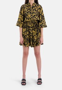 Sukienka z krótkim rękawem w kolorze żółtym z czarnym wzorem zwierzęcym. Posiada kołnierzyk, elastyczną talię oraz falbaniaste wykończenie dołu. Noszona z czarnymi sandałami.